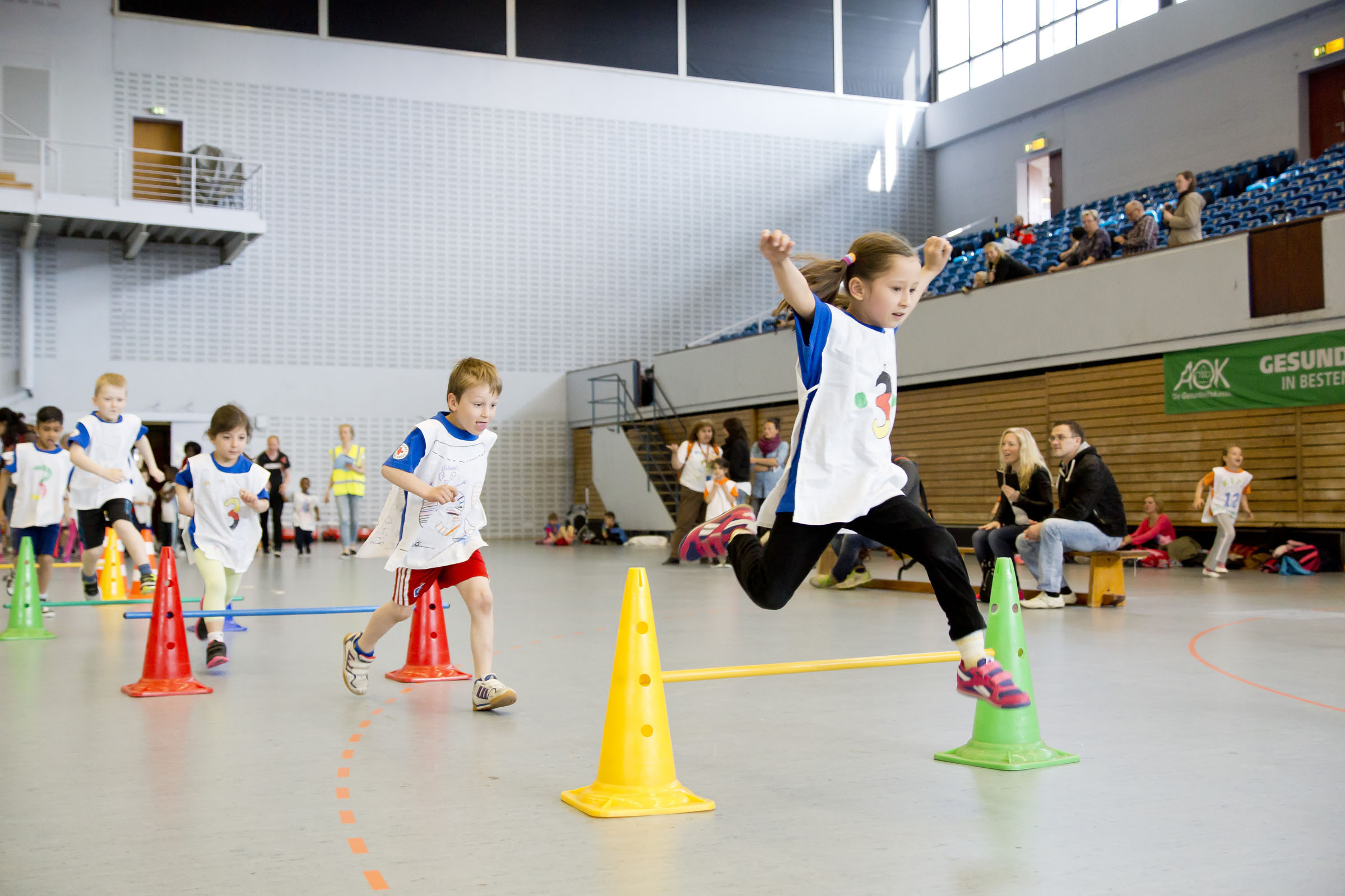Kita-Kinder fahren gemeinsam einen Bobby-Car-Parcours in einer Sporthalle