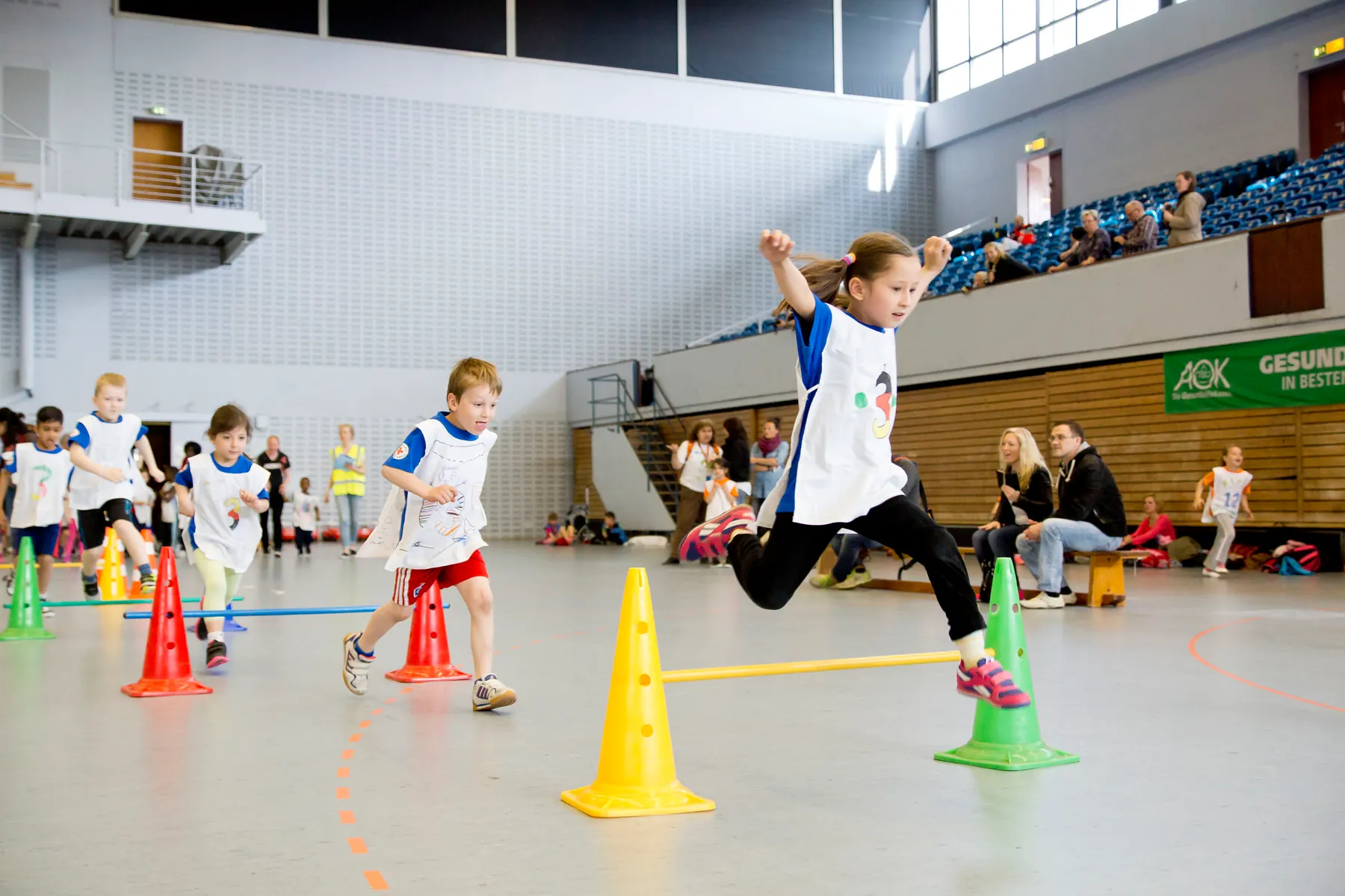 Kita-Kinder fahren gemeinsam einen Bobby-Car-Parcours in einer Sporthalle